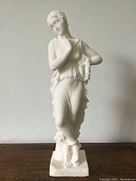 Front view of the white stone goddess statue standing on a table against a plain wall background.