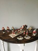 Wide view of the lot showing Santa in sleigh, skiing elves, small Santa ski figures, and two tree ornaments on wooden table.
