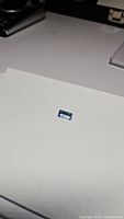 Aquamarine gemstone on white surface showing deep aqua blue color and emerald cut shape.