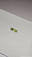 Pair of rectangular emerald cut apple green peridot gemstones lying flat on white paper background.