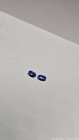 Two oval cut deep blue-purple tanzanite gemstones side by side on a white background.
