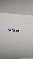 Three oval cut tanzanite gemstones arranged in a row on a plain surface, showing their deep blue and purple hues.