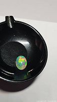 Close-up photo of the oval cabochon Ethiopian opal with visible rolling rainbow flash inside a black display dish.