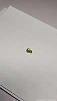 Photo showing pear cut natural yellow-green sphene gemstone on white background, highlighting its size, cut, and luster.