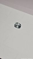 Photo showing the oval cut soft blue-green aquamarine gemstone from a side angle on a white background highlighting its clarity and color.