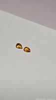 Two small pear-shaped golden yellow sapphire gemstones photographed on white background, showing color and clarity.