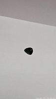 Photo of a natural forest green pear cut sapphire gemstone on a white surface, showing its size and color.
