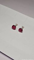 Pair of natural ruby stud earrings photographed on white paper background showing ruby gemstones and sterling silver settings.