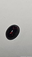 Close-up image of the jet black opal cabochon showing flashes of red and orange colors.