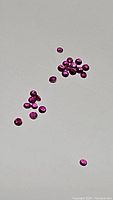 Scattered loose natural untreated round cut rubies on plain white background, showing size and color.