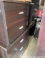 Side view of the wooden nightstand showing three drawers with silver handles and some edge wear.