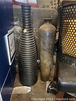Two large vases side by side, black ribbed vase on left and metal rustic vase on right, showing overall size and condition including dust and wear.