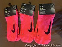 Three pairs of bright pink Nike Elite Cushioned socks with black swoosh, packaged with hang tags, laid out side by side