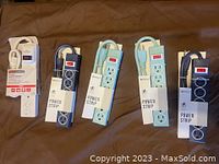 Five Vivitar power strips, three light blue and two dark blue, with packaging and cords wrapped, shown on a brown fabric background.