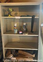 Front open view of beige metal garage storage cabinet shelf with miscellaneous small items including spray bottles, a drill, tape, and boxes inside.