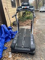 Front view of Bowflex TC200 showing tread belts and console area, placed outdoors with some leaves and a tarp visible.