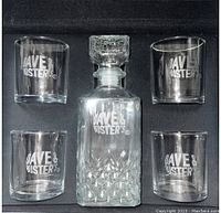 Front view of the glass decanter with diamond pattern and four matching glasses inside black box, all with Dave & Busters logo.