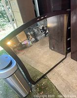 Photo of large rectangular mirror with dark wood frame, placed outdoors reflecting ground and other items.