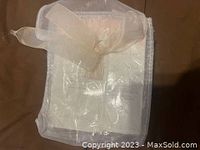 White organza pouch with translucent spatula and folded instruction sheet inside, on brown surface.