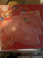 Top view of Mikasa Christmas tree-shaped platter on a red box, showing embossed holiday ornament designs on translucent glass surface with some dirt.