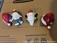 Four Christmas-themed stocking holders including Santa and snowman figures and two Santa hats on cardboard surface.