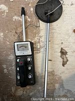 Full view of the metal detector including the handheld unit with analog meter and telescoping shaft with circular search coil.