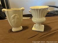 Two vintage cream-colored ceramic vases on cloth surface.