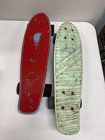 Two vintage penny skateboards side by side on white surface, one red deck, one white marbled with Kryptonics branding, showing wear and scratches.