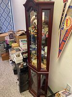 Front view of a tall dark wood curio cabinet filled with assorted items visible through glass doors.