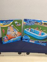 Photo showing unopened boxes of H2O GO 8ft rectangular pool and 18ft triple slide water slide, both new and sealed.