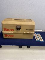 Old Pal Bass Boss 6500 beige plastic tackle box on blue cloth surface with two new packaged sinkers beside it.