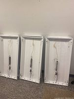 Three white rectangular fluorescent light troffers shown from the interior with ballast and wiring visible.