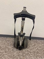 Front view of the metal golf bag carrier cart showing two wheels, adjustable straps, and foldable design.