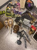 Lot of assorted Halloween decorations including skull lollipops, plastic spider decorations, skull figures, mace prop, and Halloween themed signs and packaging. Items mostly new with some used.