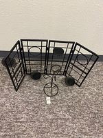 Large folding metal candle holder with three panels and multiple candle platforms shown upright on carpeted floor against a wall.
