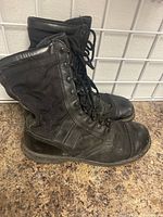 Side view of a pair of black military boots showing wear, creased leather, and scuffed toes.