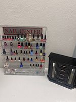 Full view of the metal nail polish display rack labeled 'NAIL CENTER' with various nail polish bottles and a black jewelry box with drawers beside it.