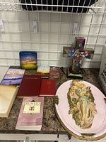 Display of various religious books including multiple Bibles and devotional books, next to decorative religious items such as a cross statue and a religious wall plaque.