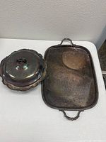 Serving tray with handles and covered dish on a table; both tarnished with patina