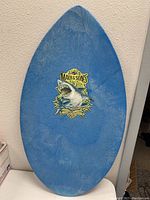 Front view of blue skim board with Maui & Sons shark logo decal in center.