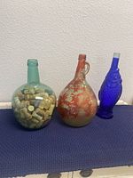 Three vintage decorative glass wine bottles on dark mat against white background