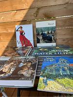 All six coffee table books displayed on a wooden table outdoors. Titles and covers visible include Monet Water Lilies, Van Gogh, Degas, and Vogue The Covers.