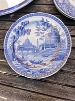 Blue and white plate with riverside cityscape showing buildings, bridge, river boats, and trees.