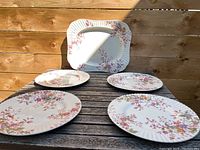 Four floral patterned round dinner plates and one rectangular platter displayed on wooden surface outdoors, showing the set arrangement and pattern.