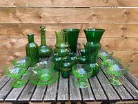 Front view of entire lot of sixteen green glass pieces on wooden table with wood panel background.