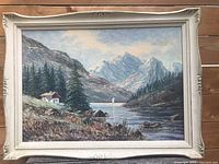 Full view of framed oil painting showing mountainous landscape with cabin, lake, and sailboat.