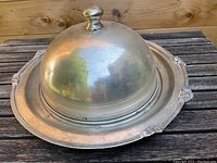 Large silver serving dish shown upright with dome lid in place, knob handle on top visible.