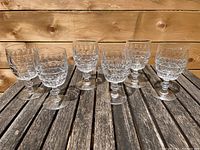 Six clear glass goblets arranged on a wooden surface showing full view of the lot.