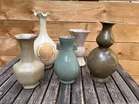 Front view of 5 assorted small ceramic vases arranged on wooden table, showing various shapes and glazes.
