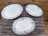 Three oval ceramic platters with blue floral border designs arranged on a wooden surface.